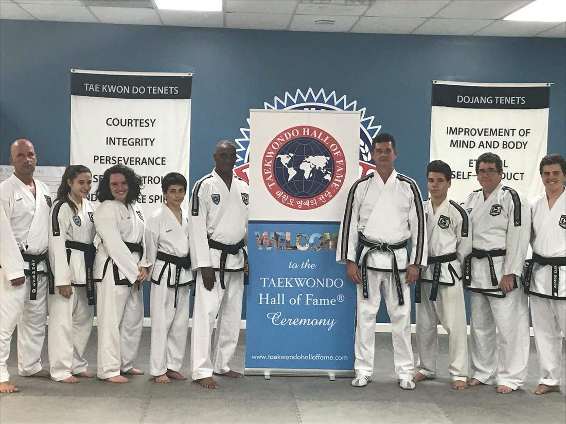Black belts of the M.J. O&rsquo;Malley Tae Kwon Do Center lined up beside a Taekwondo Hall of Fame banner in Peabody, marking Michael O&rsquo;Malley&rsquo;s 2017 induction.
